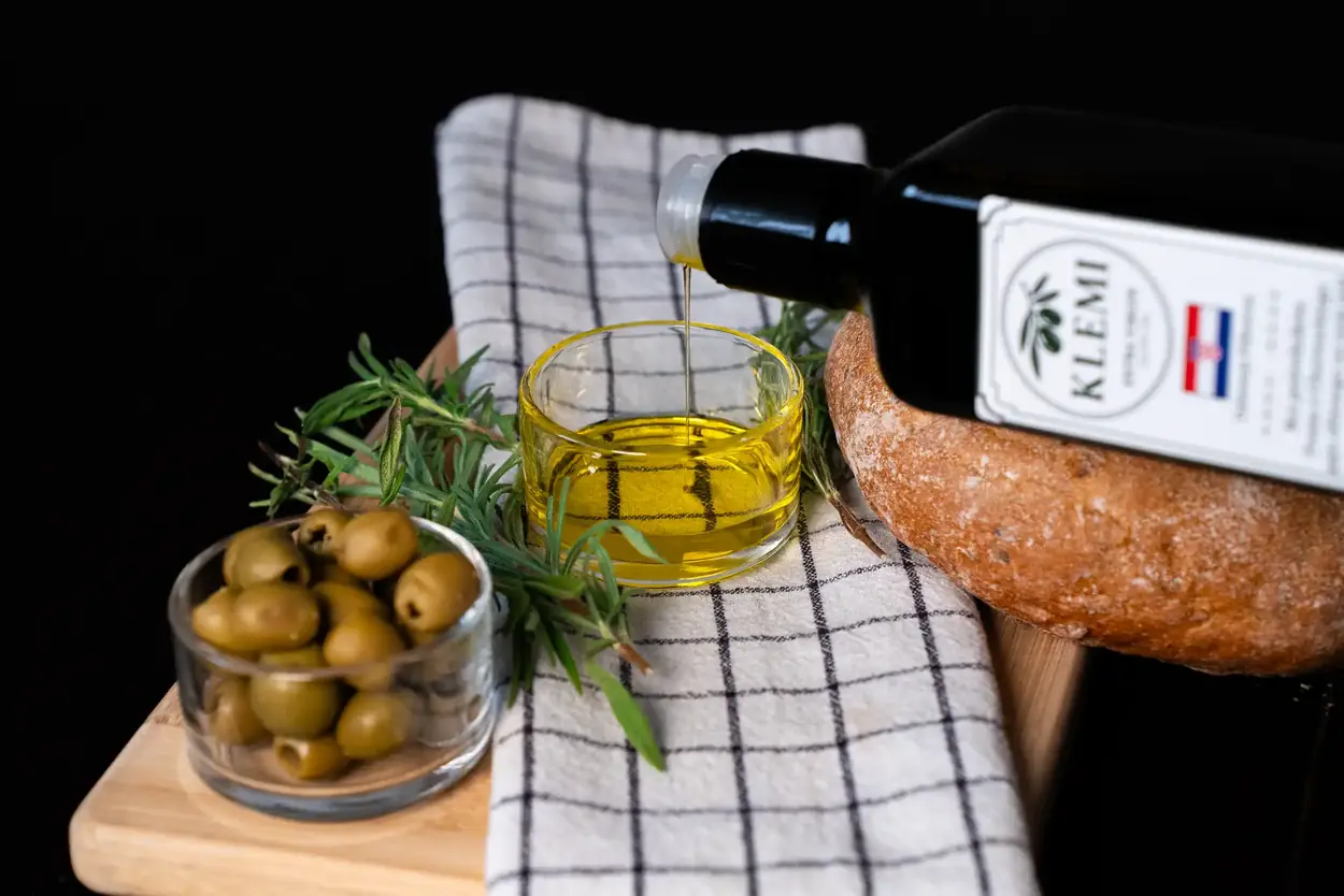 Oliwa z oliwek KLEMI nalewana do miseczki obok chleba i oliwek